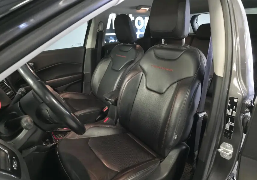 Vue intérieure côté conducteur du Jeep Compass gris, sièges cuir noirs avec logo Trailhawk brodé en rouge.