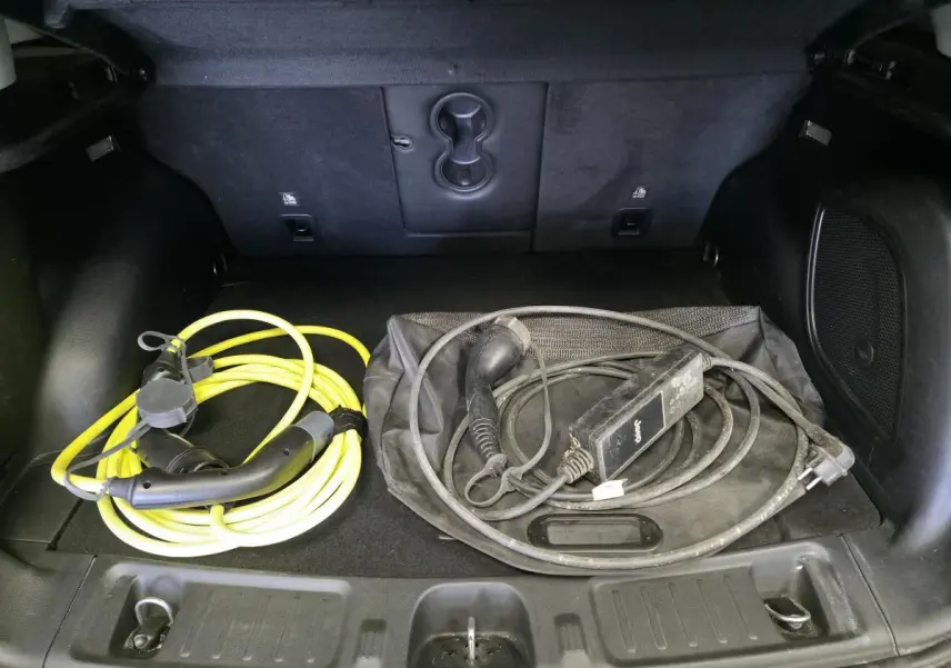 Coffre ouvert d’un Jeep Compass gris montrant deux câbles de recharge pour véhicule hybride rechargeable.