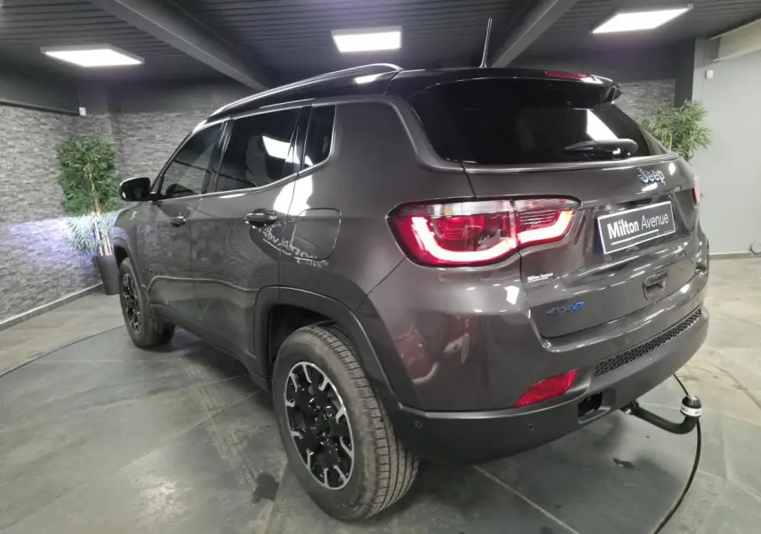 Vue 3/4 arrière droite du Jeep Compass gris métallisé avec attelage fixe et toit noir dans un showroom.