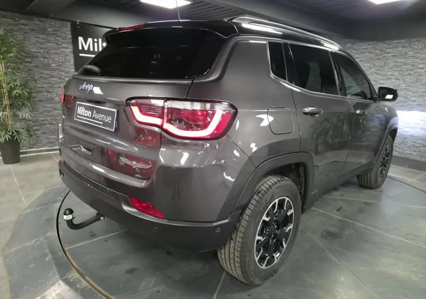 Jeep Compass gris métallisé en 3/4 arrière droit avec attelage fixe et toit noir dans un showroom.
