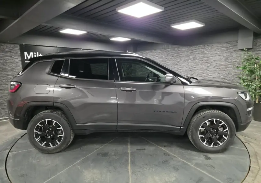 Vue de profil côté gauche d'un Jeep Compass gris métallisé avec toit noir, roues noires et détails Trailhawk.