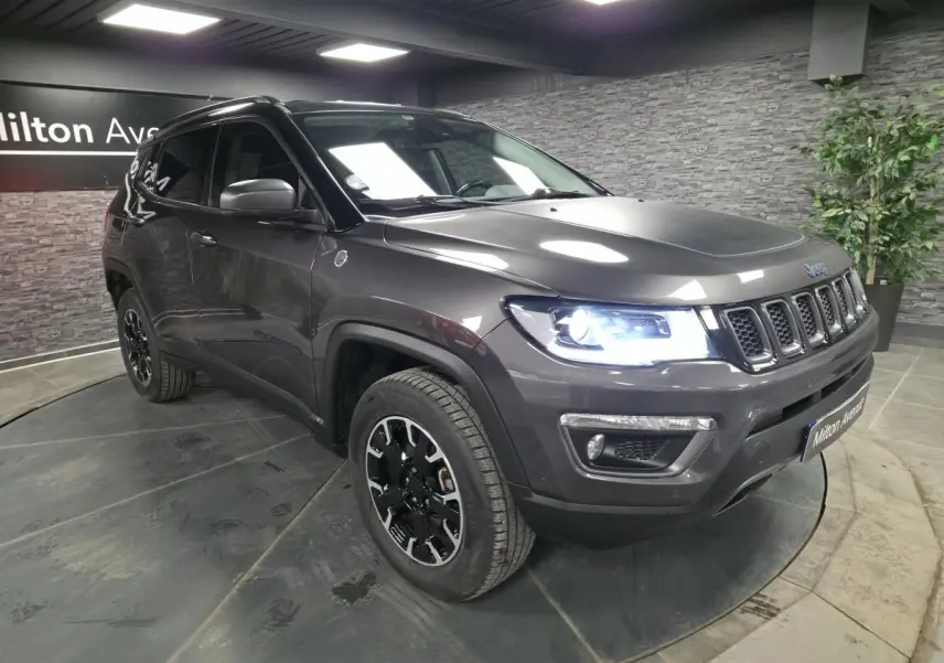 Jeep Compass gris métallisé en 3/4 avant droit avec phares allumés dans un showroom intérieur.