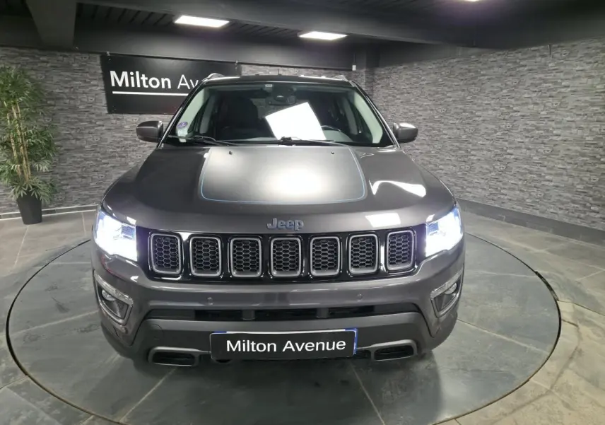 Vue de face du Jeep Compass gris métallisé avec calandre distinctive et phares allumés dans un showroom.