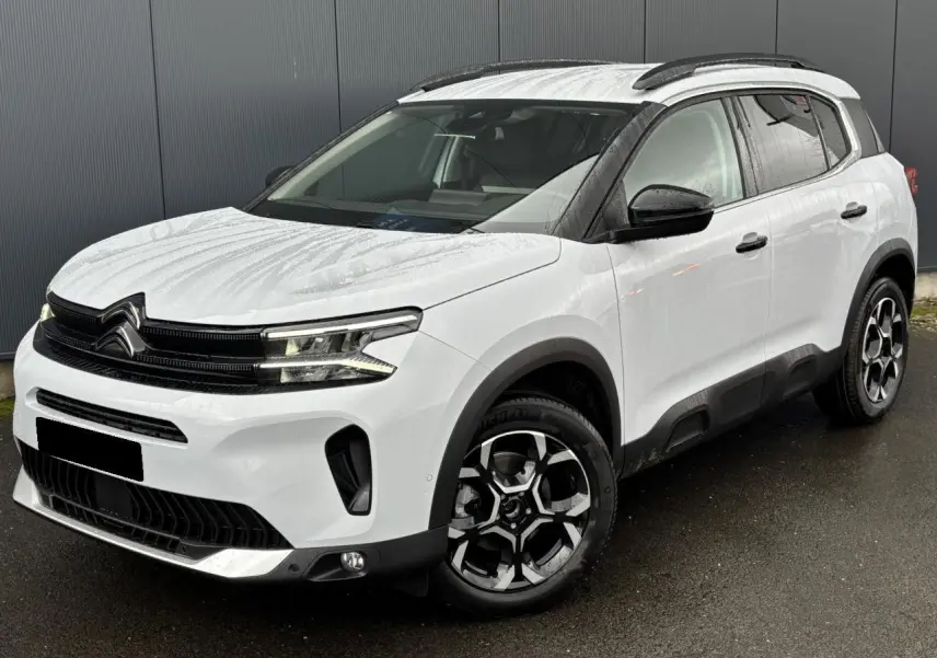 Vue 3/4 avant droite d'un Citroën C5 Aircross blanc Okénite avec jantes alliage bi-ton et barres de toit noires.