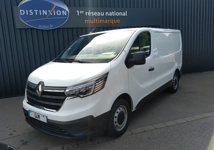 Renault Trafic Fourgon blanc en 3/4 avant droit, avec calandre noire et jantes acier, stationné devant un mur gris.