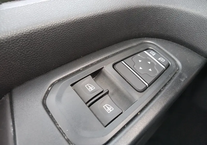 Gros plan sur les commandes de lève-vitres et réglage des rétroviseurs côté conducteur du Renault Trafic Fourgon blanc.