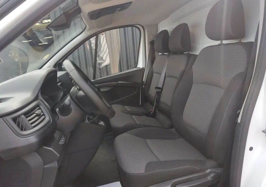 Vue intérieure côté conducteur du Renault Trafic Fourgon blanc 2024, montrant les sièges tissu gris et le volant multifonction.