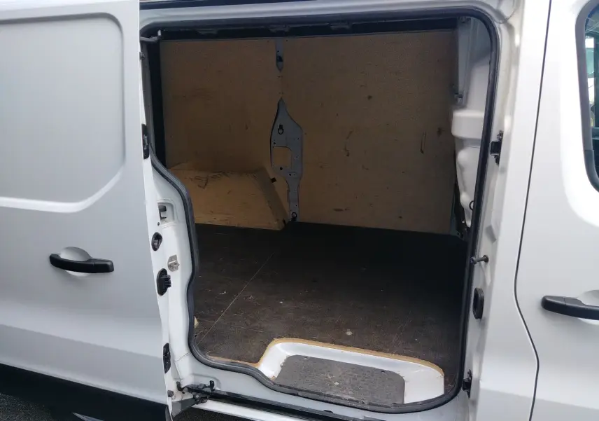 Vue intérieure du fourgon blanc Renault Trafic avec porte latérale ouverte, montrant l'espace de chargement vide.