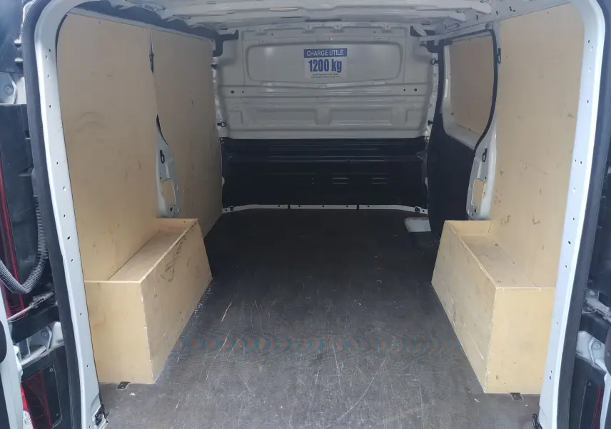 Vue intérieure arrière du Renault Trafic Fourgon blanc 2024, montrant l'espace de chargement avec panneaux bois et capacité 1200 kg.