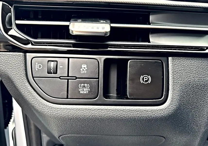 Gros plan sur les commandes noires du tableau de bord du Kia Sportage 1.6 hybride blanc, avec bouton frein à main électronique.