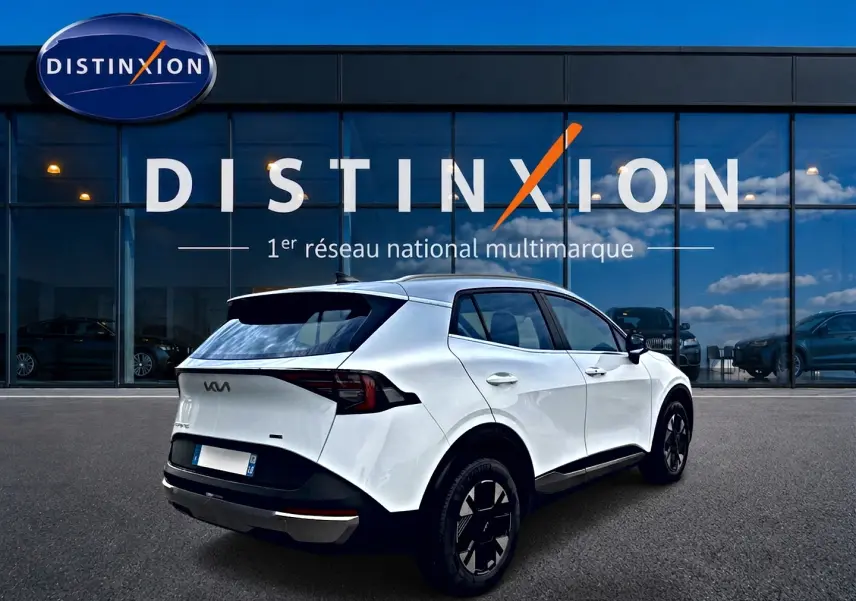 Vue 3/4 arrière droite d'un KIA Sportage 1.6 hybride blanc, avec jantes noires et toit noir devant une vitrine Distinxion.