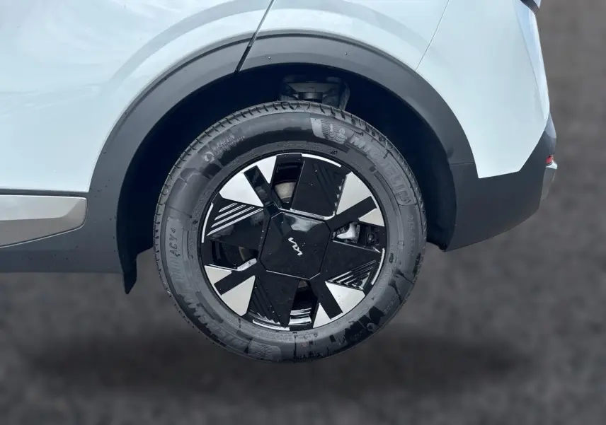 Gros plan sur la roue arrière droite blanche du Kia Sportage 1.6 hybride 239 avec jante alu noire et argentée au design géométrique.
