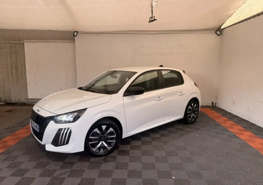 Peugeot 208 blanche vue en 3/4 avant droit dans un garage avec jantes noires et phares LED allumés.