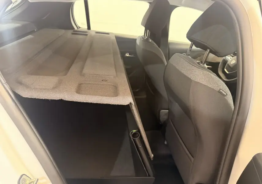 Vue intérieure côté droit de la Peugeot 208 blanche 2025, montrant les sièges avant et le coffre avec cache-bagages relevé.
