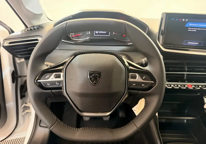 Vue rapprochée du volant cuir noir de la Peugeot 208 blanche, avec tableau de bord et écran tactile central visibles.