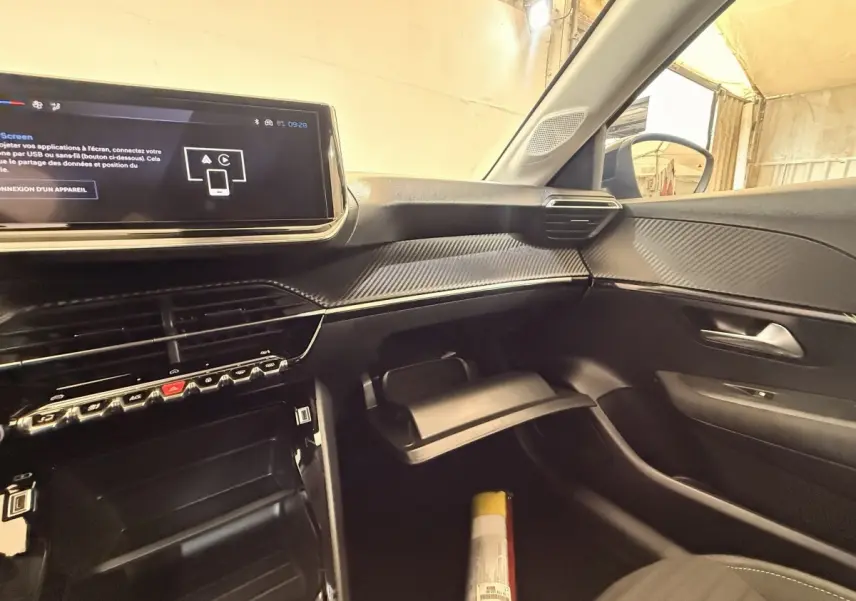 Intérieur de la Peugeot 208 blanc, vue côté passager, tableau de bord moderne avec écran tactile et boîte à gants ouverte.