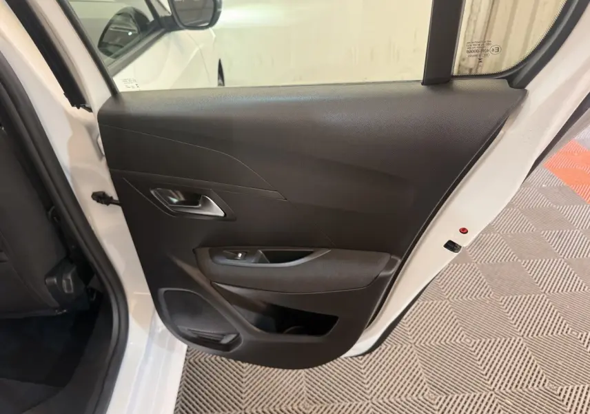 Vue intérieure de la porte arrière droite ouverte d'une Peugeot 208 blanche, avec panneau noir et poignée intégrée.
