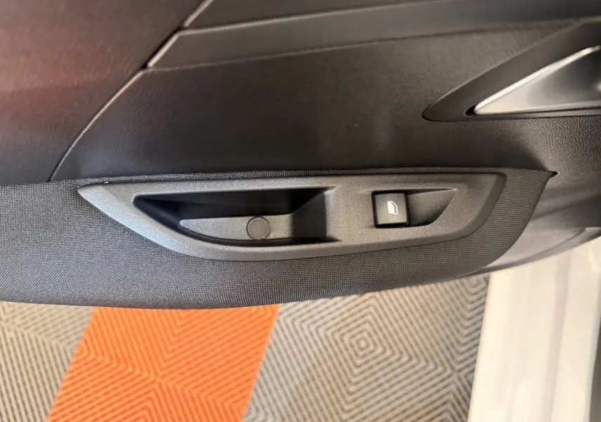 Gros plan sur la commande de lève-vitre côté conducteur d’une Peugeot 208 blanche, intérieur noir.