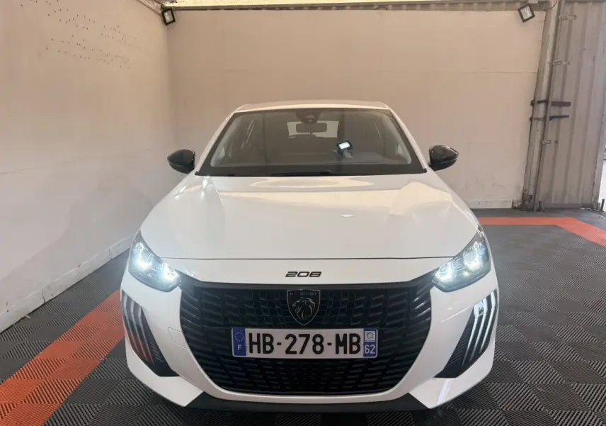 Vue frontale d'une Peugeot 208 blanche 2025 avec phares allumés et calandre noire distinctive.