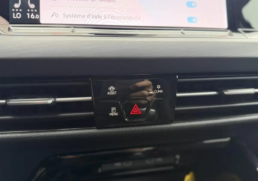 Gros plan sur la console centrale noire avec boutons d'alerte et d'assistance de la Volkswagen Golf VIII blanche.