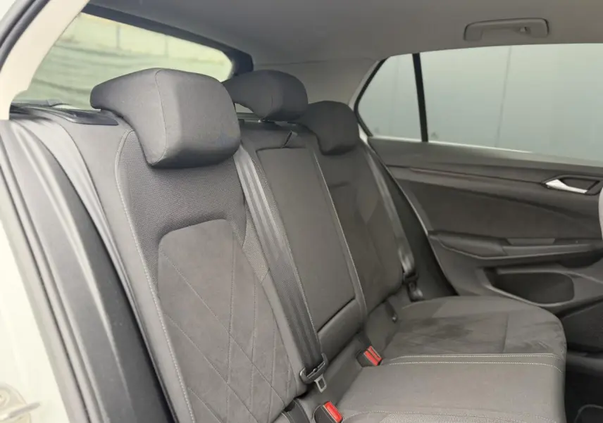Vue intérieure côté arrière droit montrant les sièges arrière en tissu microfleece gris foncé de la Volkswagen Golf VIII blanche.
