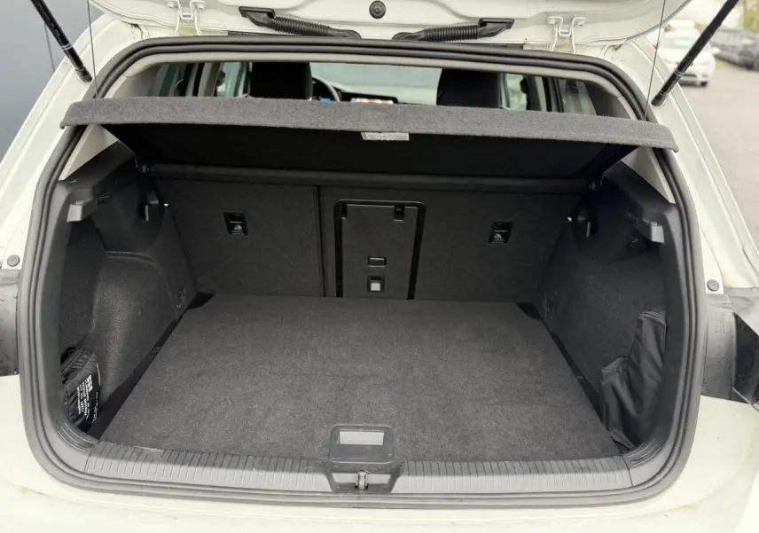 Coffre ouvert vu de l'arrière d'une Volkswagen Golf VIII 1.5 TSI blanche, montrant l'espace de chargement vide et la tablette arrière.