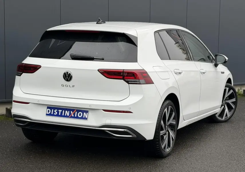 Vue 3/4 arrière droite d'une Volkswagen Golf VIII blanche avec jantes alliage 18 pouces et vitres arrière surteintées.