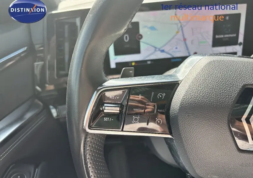 Gros plan sur le volant du Renault Austral 2024, avec commandes intégrées et écran tactile flou en arrière-plan.