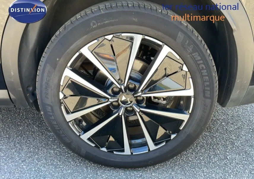 Gros plan sur la jante noire et argentée d’un DS7 2024 noir métal avec pneu Michelin sur sol goudronné.