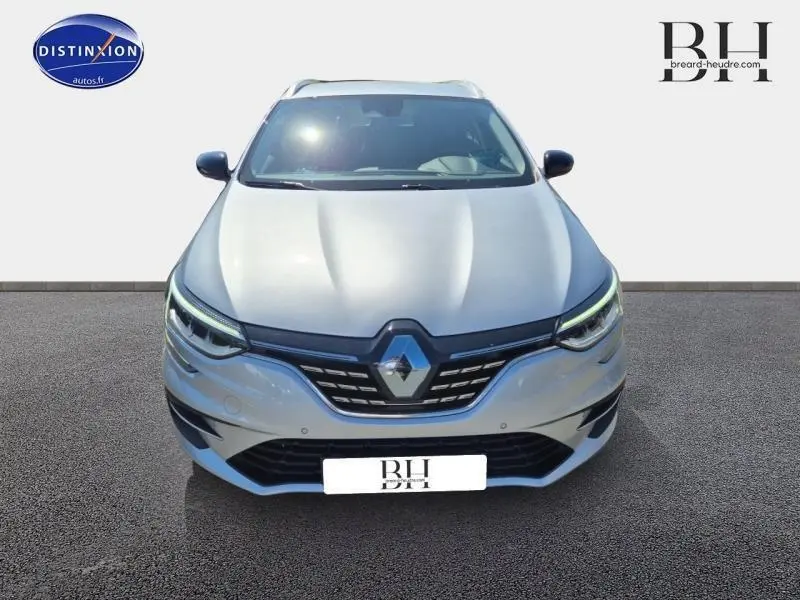 Vue frontale d'une Renault Mégane Break gris titanium 2024 avec calandre noire et phares LED allumés.