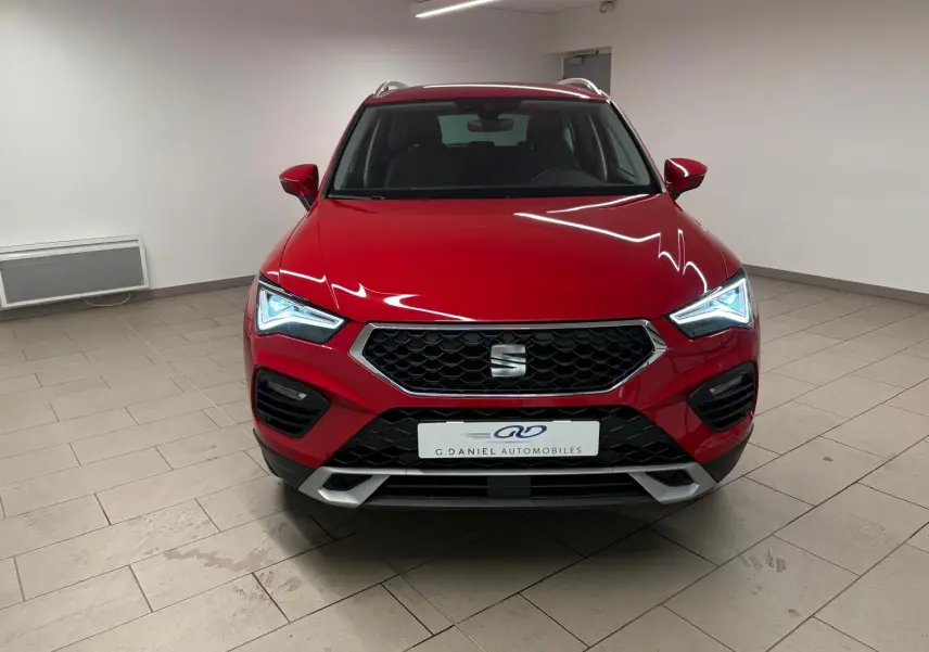 Vue de face du SEAT Ateca 2024 en Rouge Velvet métallisé avec phares allumés dans un intérieur neutre.