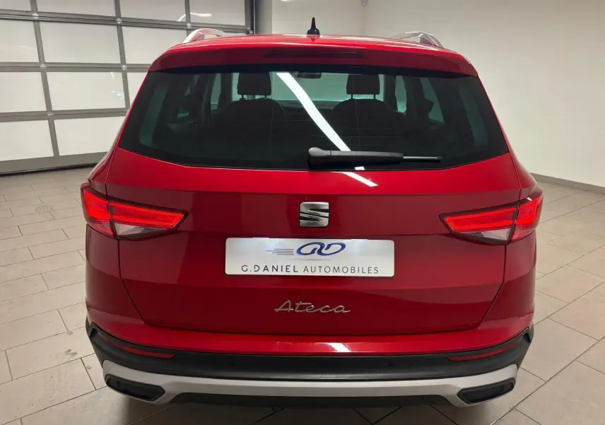 Vue arrière d'un SEAT Ateca Rouge Velvet 2024, mettant en valeur les feux allumés et le logo central sur fond métallique.