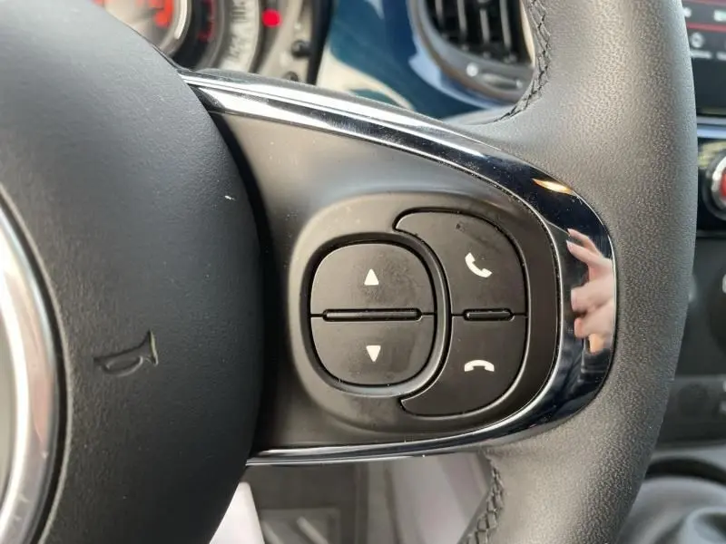 Gros plan sur les commandes du volant côté droit d'une Fiat 500 bleu métal 2023, avec boutons de téléphone et volume.