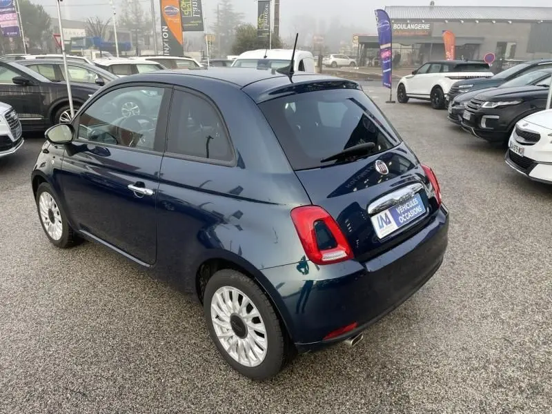 Vue 3/4 arrière droite d'une Fiat 500 bleu métal 2023, compacte et élégante, avec jantes argentées et vitres teintées.