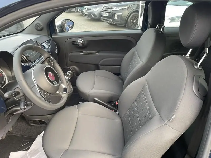 Intérieur de la Fiat 500 2023 vu côté conducteur, sièges gris, volant multifonction et tableau de bord bleu métal.
