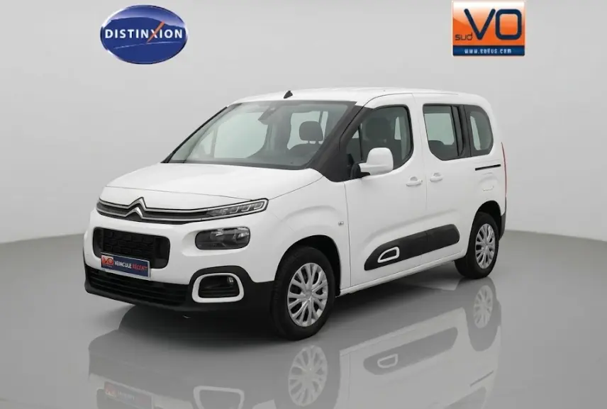 Citroën Berlingo blanc vue 3/4 avant droit avec protections latérales noires et barres de toit visibles.