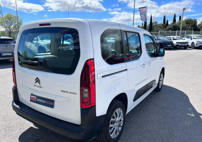 Vue 3/4 arrière droite du Citroën Berlingo blanc avec barres de toit et protections latérales noires.