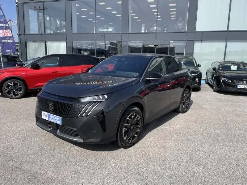 Peugeot 3008 Nouveau gris foncé en 3/4 avant droit, avec calandre noire et jantes noires brillantes, stationné devant un showroom.