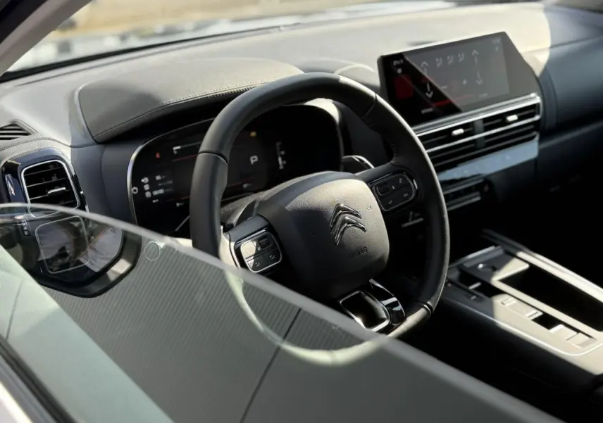 Vue intérieure du poste de conduite du Citroën C5 Aircross 2025, volant cuir noir et écran tactile central.