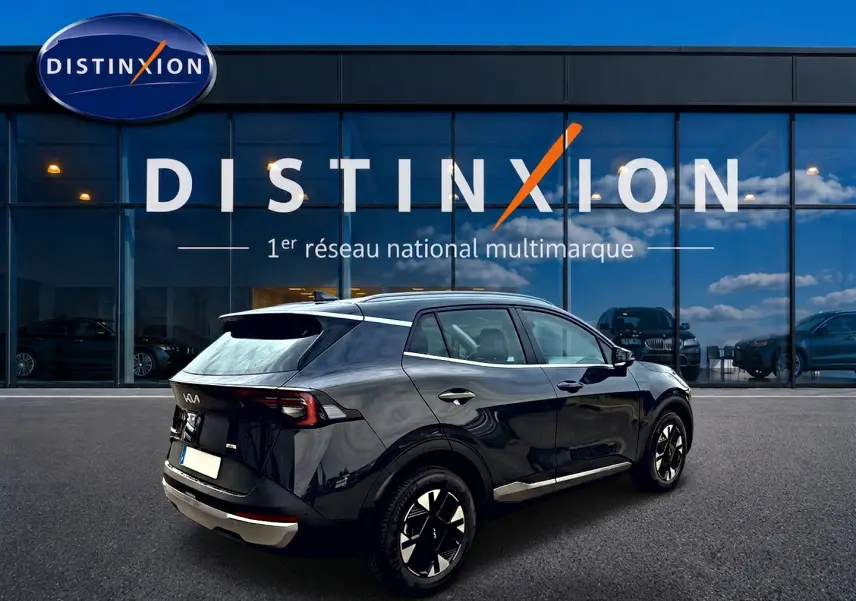 KIA SPORTAGE 1.6 hybride 239 gris eclipse vu en 3/4 arrière droit devant un showroom Distinxion.