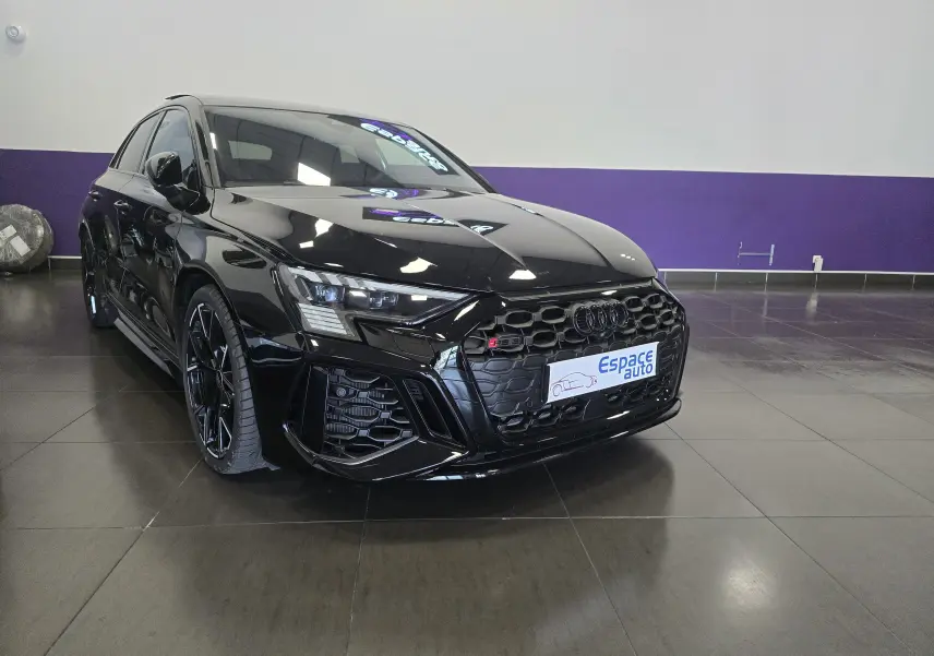 Audi RS3 Sportback noir vue 3/4 avant droit, avec calandre hexagonale et jantes noires distinctives.