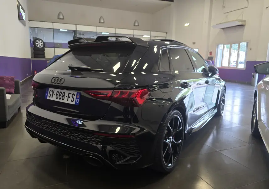 Audi RS3 Sportback noir vue 3/4 arrière droit en intérieur, avec jantes noires et feux arrière LED distinctifs.