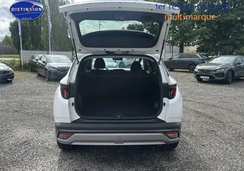 Vue arrière d'un Hyundai Tucson blanc sérénité 2025 avec coffre ouvert sur un parking extérieur.