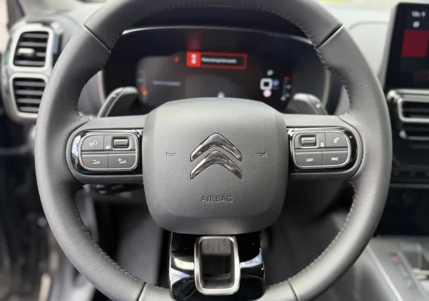 Gros plan sur le volant en cuir noir du Citroën C5 Aircross 2025 avec commandes intégrées et logo chromé central.