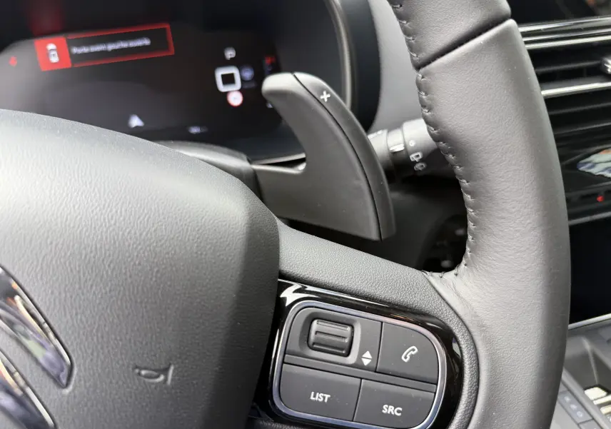 Gros plan sur le volant en cuir noir et la commande multifonction du Citroën C5 Aircross 2025, tableau de bord numérique en arrière-plan.