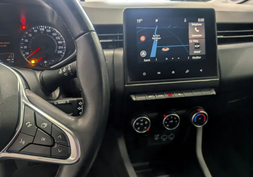 Vue rapprochée de l'intérieur de la Renault Clio V TCe 100 Business, montrant le volant, l'écran tactile et les commandes de climatisation.