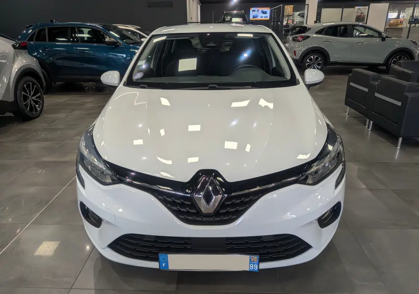 Vue de face d'une Renault Clio V TCe 100 Business en Blanc Glacier, éclairage showroom soulignant sa calandre noire brillante.