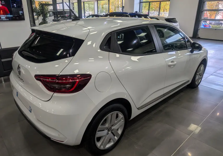 Renault Clio V TCe 100 Business blanc Glacier vue 3/4 arrière droit en showroom lumineux.
