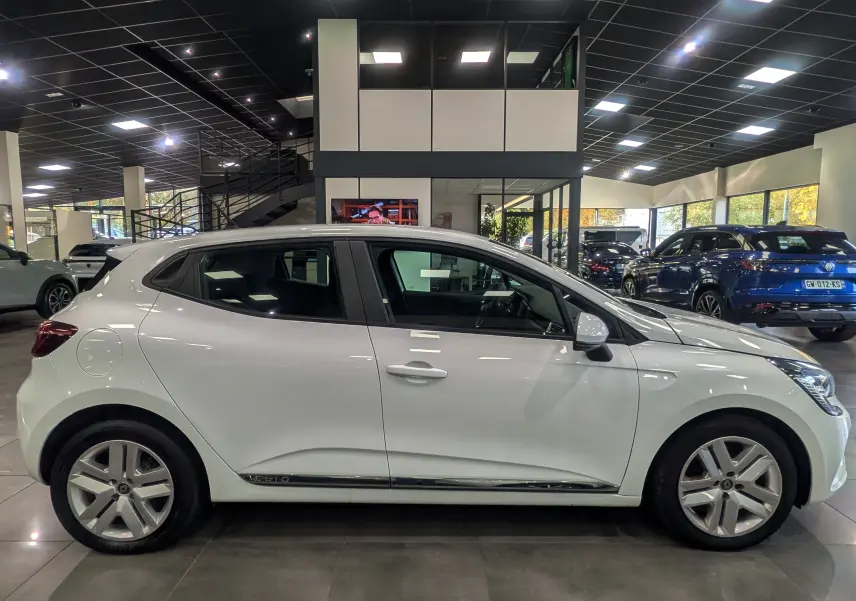 Profil côté gauche d'une Renault Clio V blanche Glacier, version TCe 100 CH BUSINESS, en intérieur showroom.