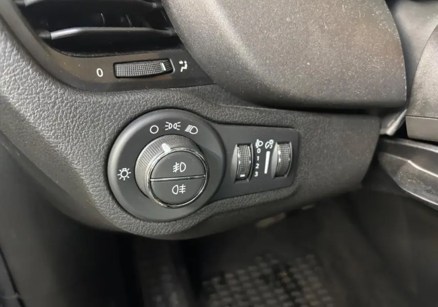 Gros plan sur la molette des phares et commandes d’éclairage du tableau de bord d’une FIAT 500X gris MY23.